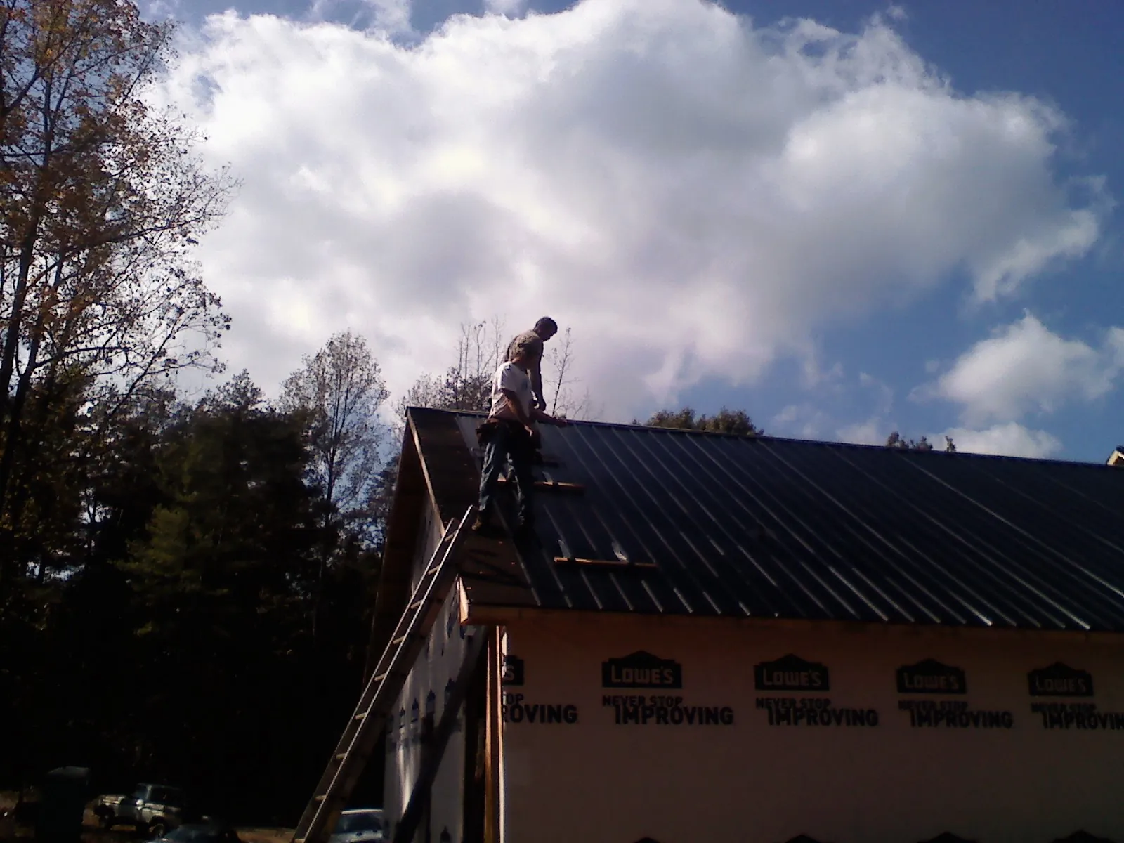 Roofer fastening dark metal panels high against a cloudy sky in Plymouth